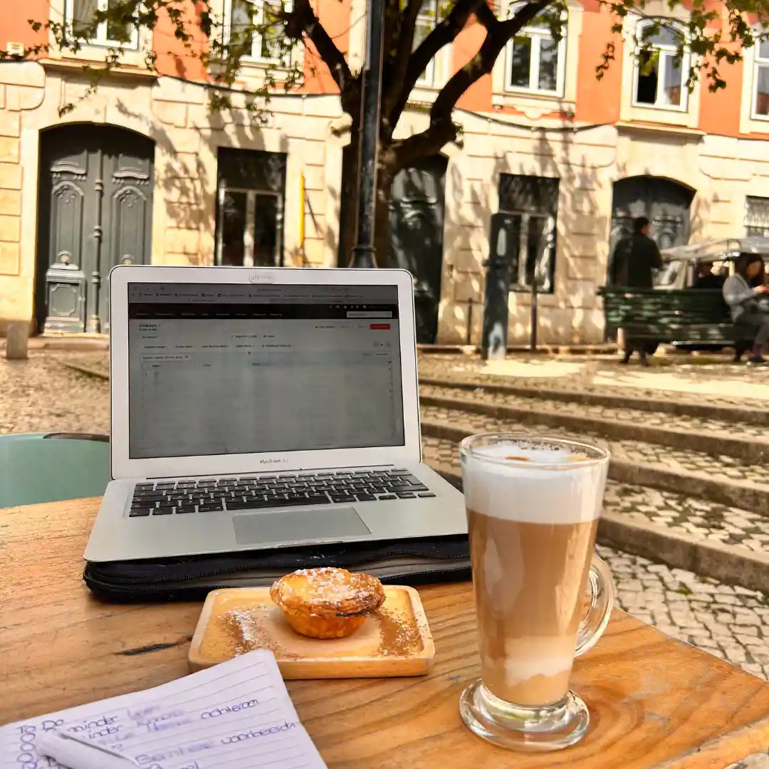 Macbook met latte macchiato en pastel de nata op een terras tafeltje in een stad